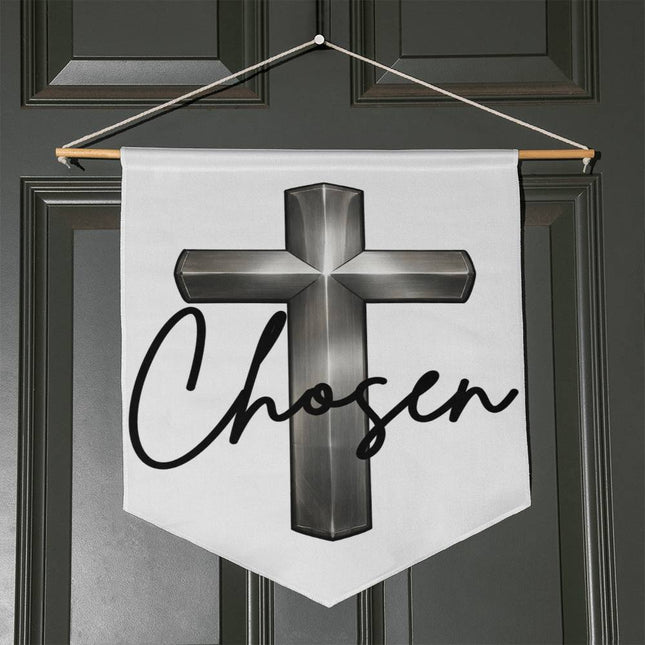White pennant-shaped wall hanging with a silver chrome 3D cross graphic and the word "Chosen" in black script, hung with a wooden dowel and twine on a dark door.