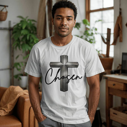 Man wearing a white unisex t-shirt featuring a silver chrome 3D cross graphic with the word "Chosen" in black script on the front, styled in a modern home setting.