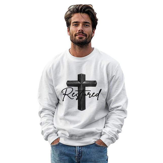 Man wearing a white unisex crewneck sweatshirt featuring a carbon-fiber black cross graphic with the word "Restored" in black script on the front, styled against a clean white background.