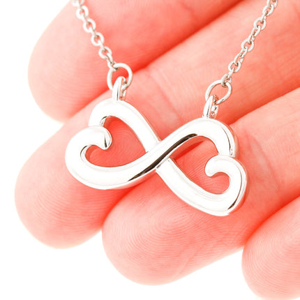 Heart-shaped infinity endless love necklace in white gold finish held in hands, displayed in a gift box with a Dearest Sister Happy Mother's Day message card on a pink floral background.
