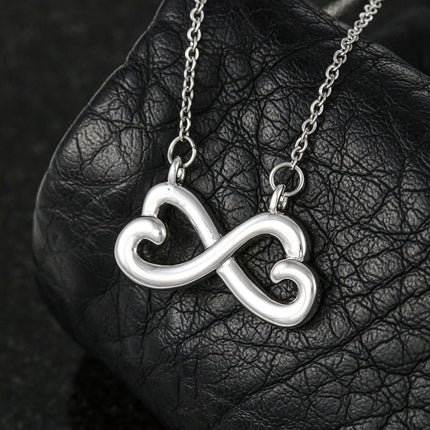 Heart-shaped infinity endless love necklace in white gold finish held in hands, displayed in a gift box with a Dear Mother-in-Law Happy Mother's Day message card and sunflower floral background.
