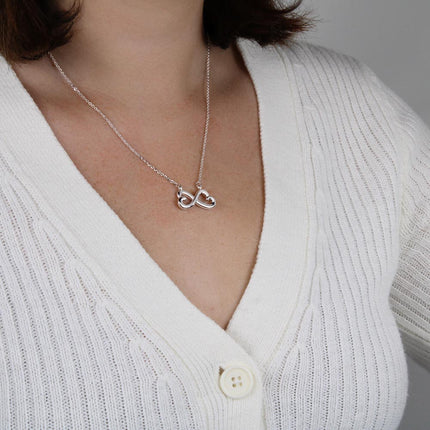 Heart-shaped infinity endless love necklace in white gold finish held in hands, displayed in a gift box with a Dear Mother-in-Law Happy Mother's Day message card and sunflower floral background.