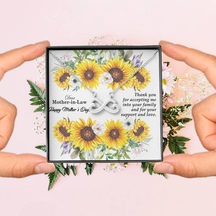 Heart-shaped infinity endless love necklace in white gold finish held in hands, displayed in a gift box with a Dear Mother-in-Law Happy Mother's Day message card and sunflower floral background.