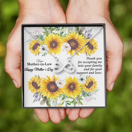 Heart-shaped infinity endless love necklace in white gold finish held in hands, displayed in a gift box with a Dear Mother-in-Law Happy Mother's Day message card and sunflower floral background.