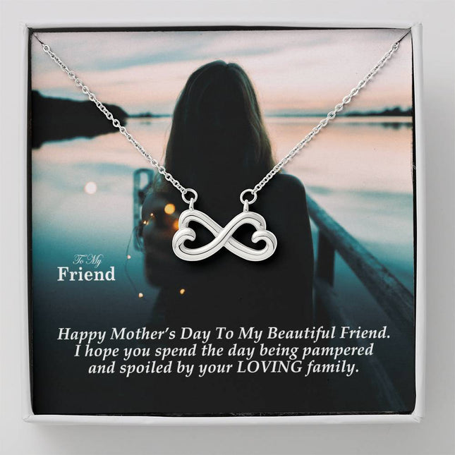 Heart-shaped infinity endless love necklace in white gold finish held in hands, displayed in a gift box with a To My Friend Happy Mother's Day message card and moody teal sunset background.