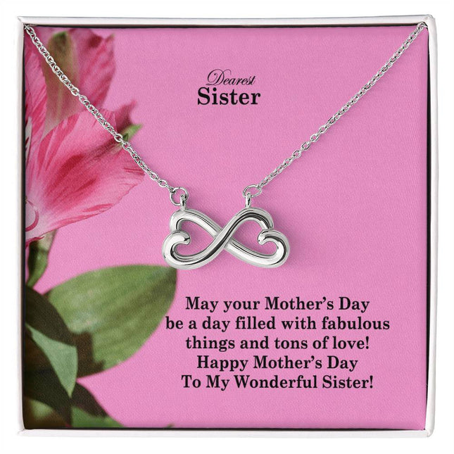 Heart-shaped infinity endless love necklace in white gold finish held in hands, displayed in a gift box with a Dearest Sister Happy Mother's Day message card on a pink floral background.