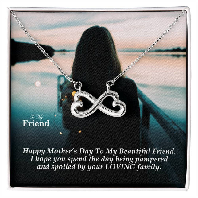 Heart-shaped infinity endless love necklace in white gold finish held in hands, displayed in a gift box with a To My Friend Happy Mother's Day message card and moody teal sunset background.