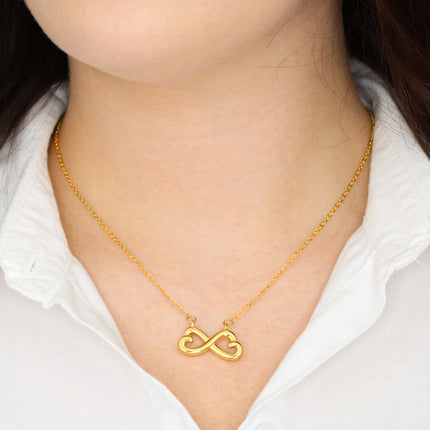 Heart-shaped infinity endless love necklace in white gold finish held in hands, displayed in a gift box with a To My Friend Happy Mother's Day message card and moody teal sunset background.