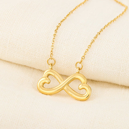 Heart-shaped infinity endless love necklace in white gold finish held in hands, displayed in a gift box with a Dearest Sister Happy Mother's Day message card on a pink floral background.
