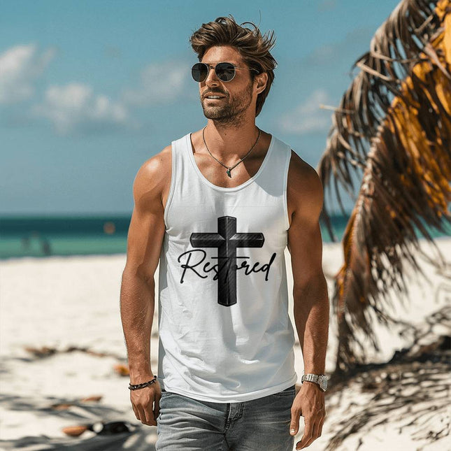 Man wearing a white unisex tank top featuring a carbon-fiber black cross graphic with the word "Restored" in black script on the front, styled on a sunny beach setting.