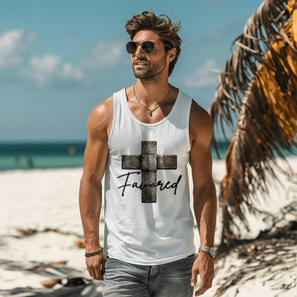 Man wearing a white unisex tank top featuring a vintage stone-tile riveted cross graphic with the word "Favored" in black script on the front, styled on a sunny beach setting.