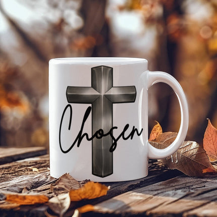 White ceramic coffee mug with a silver chrome 3D cross graphic and the word "Chosen" in black script, displayed on a rustic wooden surface surrounded by autumn leaves.