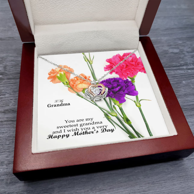 Sterling silver and rose gold crown pendant necklace with a sparkling cubic zirconia center, displayed in a mahogany luxury LED gift box with a To My Grandma Happy Mother's Day message card and colorful carnation flowers.