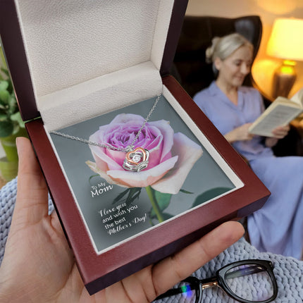 Sterling silver and rose gold crown pendant necklace with a sparkling cubic zirconia center, displayed in a mahogany luxury LED gift box with a To My Mom I Love You Happy Mother's Day message card and a pink rose background.